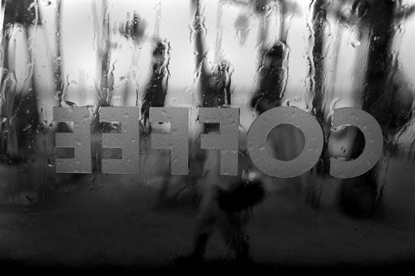 Reversed coffee shop sign on rainy window in black and white