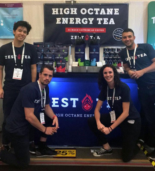 Zest Tea team of four at trade show booth with High Octane Energy Tea banner