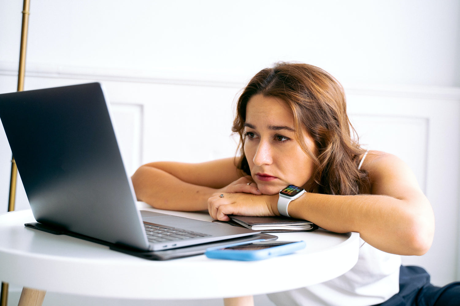 Woman resting her head on arms looking tired at laptop screen