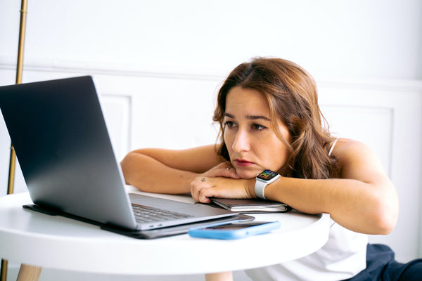 Woman resting her head on arms looking tired at laptop screen