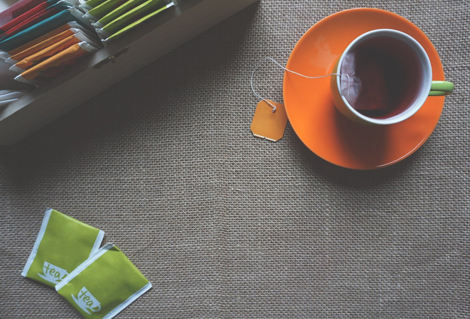 Cup of brewed tea on orange saucer with tea bags on burlap background