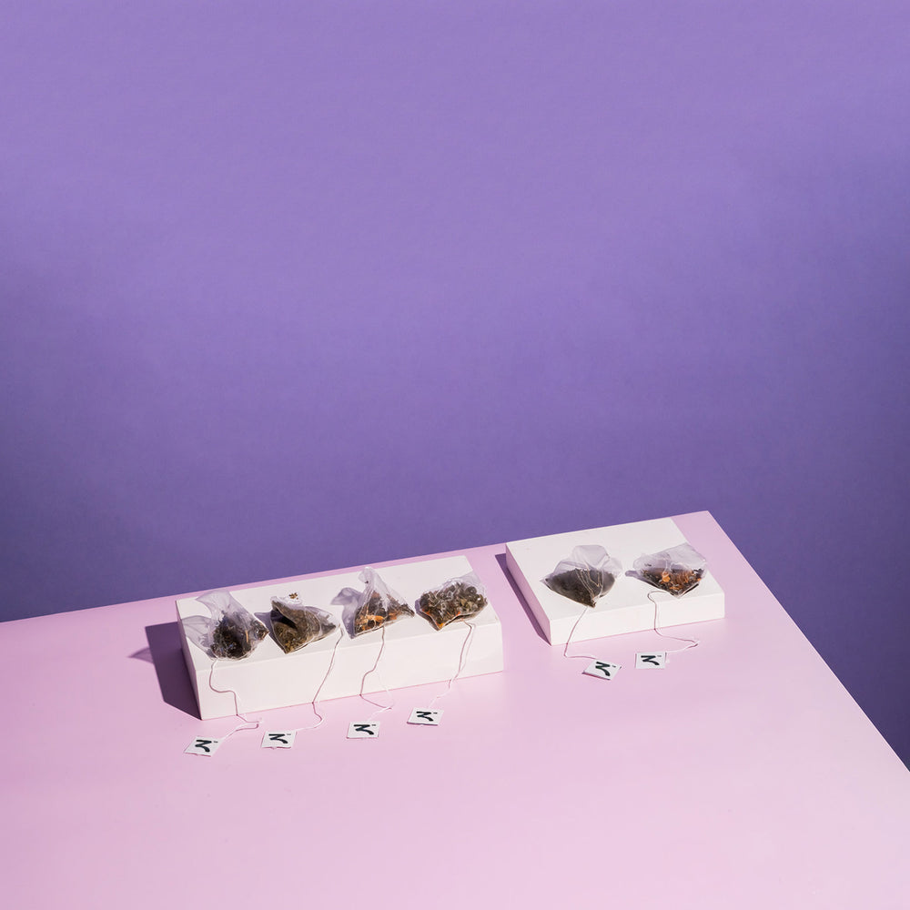 Six Zest Tea pyramid tea bags displayed on white blocks on purple background