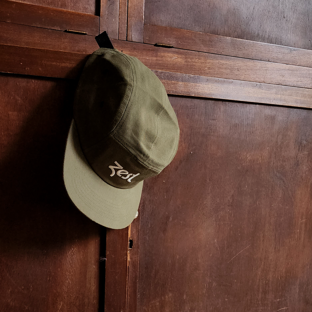 Olive green Zest five-panel cap hanging on dark wooden cabinet door