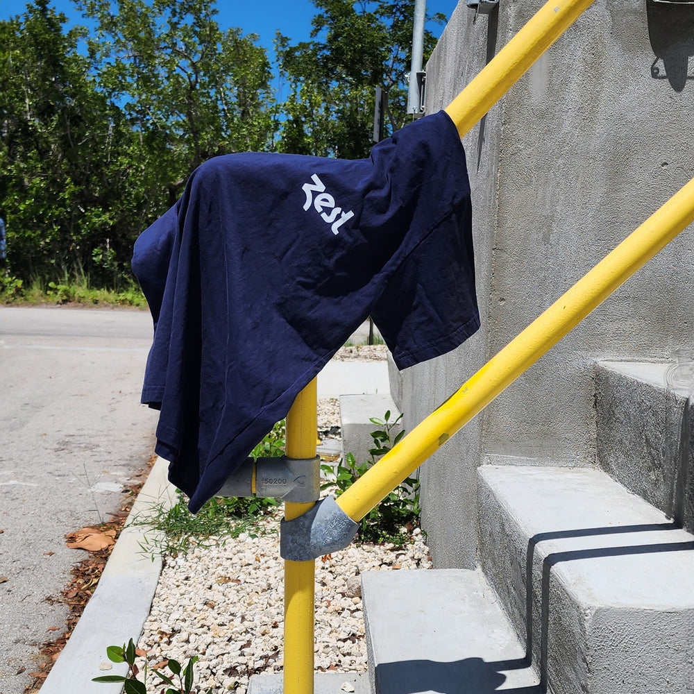 Navy Zest t-shirt draped over yellow railing outdoors on sunny day