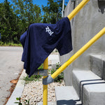 Navy Zest t-shirt draped over yellow railing outdoors on sunny day