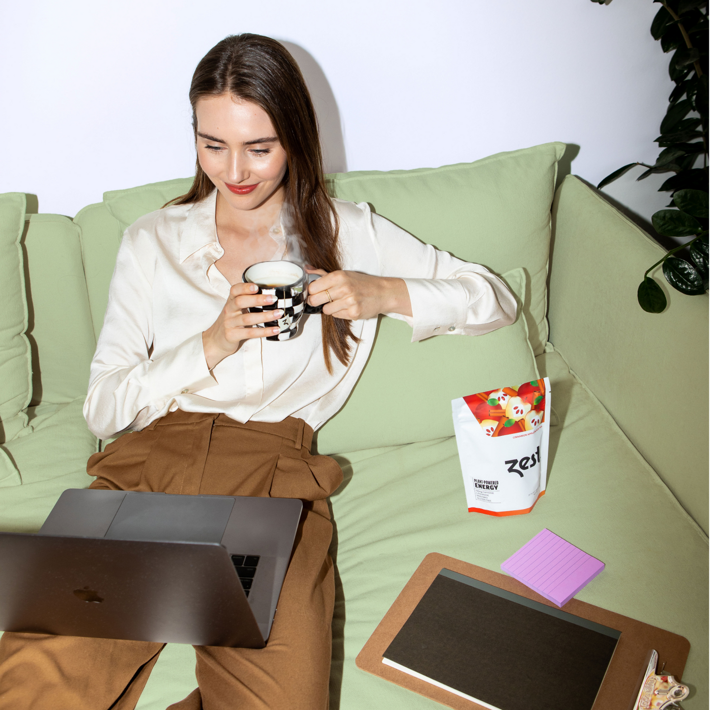 Woman on couch holding mug with Zest pouch, laptop work-from-home lifestyle