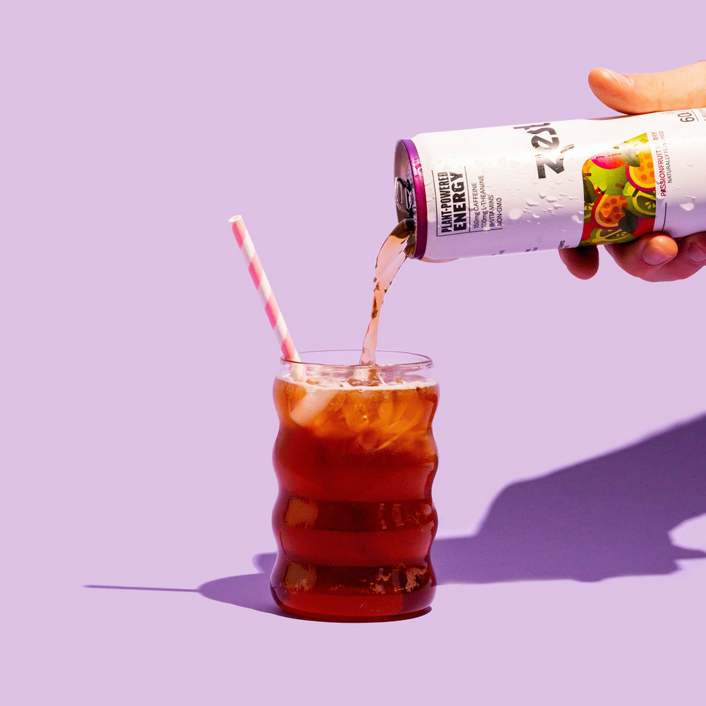 Hand pouring Zest Passionfruit Berry sparkling tea into glass with ice on purple background