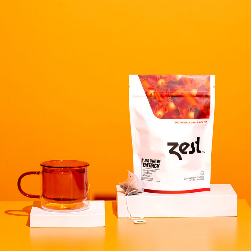 Zest Spicy Masala Chai pouch with brewed chai in amber glass mug on orange background
